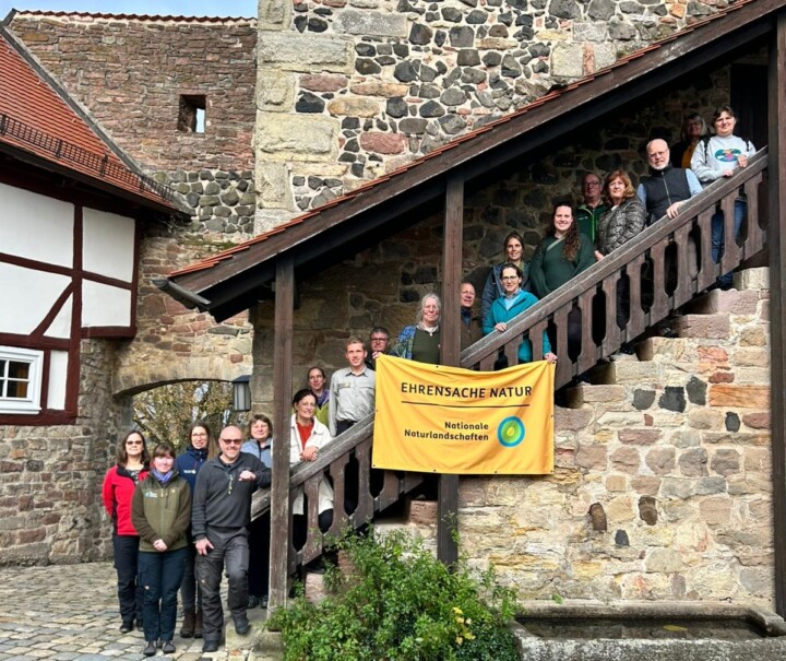Rund 20 Erwachsene stehen auf einer Treppe, eingefasst in eine alte Mauer, vor sich ein Banner "Ehrensache Natur"
