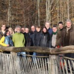 Mehrere Personen stehen, einen herbstlichen Wald im Hintergrund, auf einer Holzbrücke und schauen gut gelaunt in die Kamera