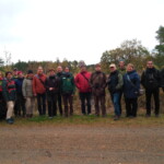 Gruppe mit ca. 20 Personen steht in einer Reihe mit Blick zur Kamera, im Hintergrund Bäume