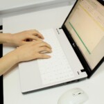 Aufgeklappter Laptop mit zwei Händen auf der Tastatur