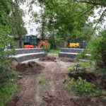Fahrspuren und Sitzmauern in Gartenbereich, im Hintergrund Kleinbagger
