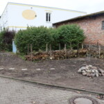 Fläche mit Lesesteinhaufen und Totholzhaufen zwischen Straße und Gebäuden