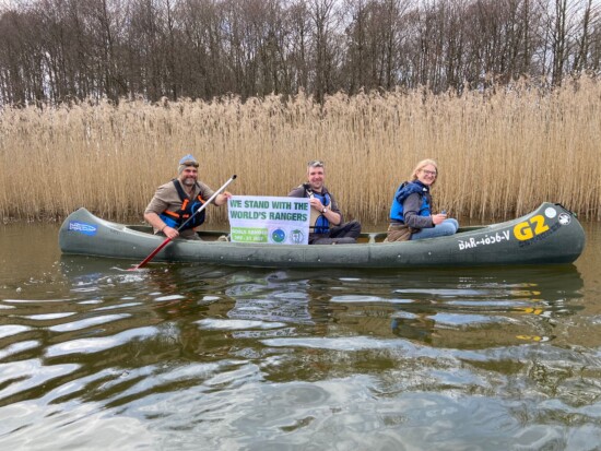 Drei Personen in einem Kanu präsentieren ein Banner mit dem Text "We stand with the world's rangers"