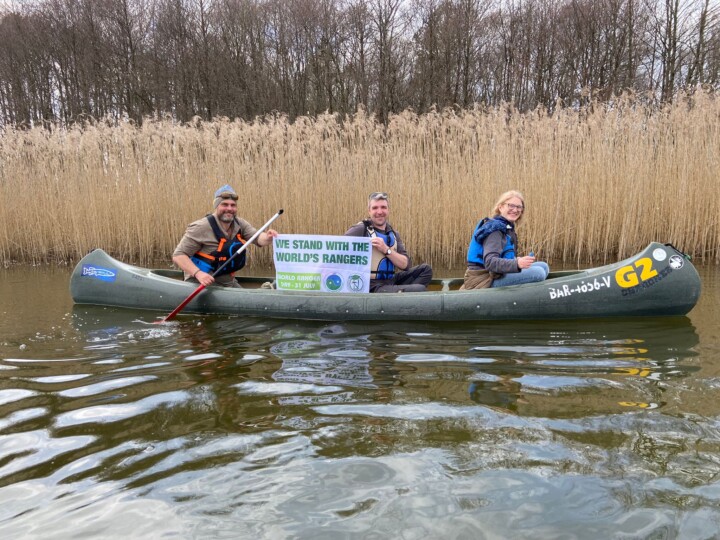 Drei Personen in einem Kanu präsentieren ein Banner mit dem Text "We stand with the world's rangers"