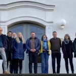 Vor einer Hauswand eines historischen Gebäudes stehen Menschen zu einem Gruppenfoto zusammen.
