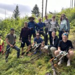 Fröhlich in die Kamera blickende Gruppe von elf Erwachsenen mit Astscheren und Arbeitshandschuhen an einem Hang, im Hintergrund Wald.