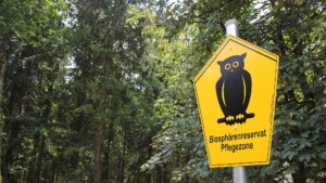 Im Vordergunf ein Biosphärenreservat-Pflegezone-Schild, im Hintergrund ist Wald zu sehen