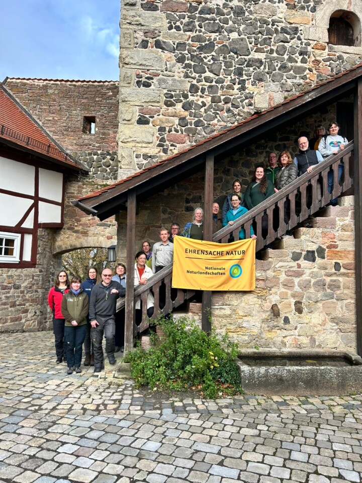 Rund 20 Erwachsene stehen auf einer Treppe, eingefasst in eine alte Mauer, vor sich ein Banner "Ehrensache Natur".