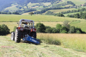 Ein Trecker mit Balkenmäher bei der Arbeit in einer hügeligen und grünen Landschaft.
