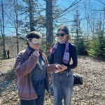 Eine Umweltpraktikantin mit verbundenen Augen wird von einer anderen Umweltpraktikantin durch den Wald geführt