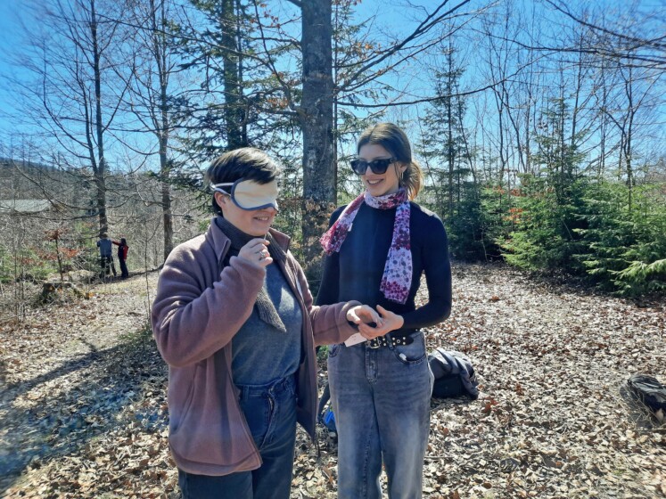 Eine Umweltpraktikantin mit verbundenen Augen wird von einer anderen Umweltpraktikantin durch den Wald geführt