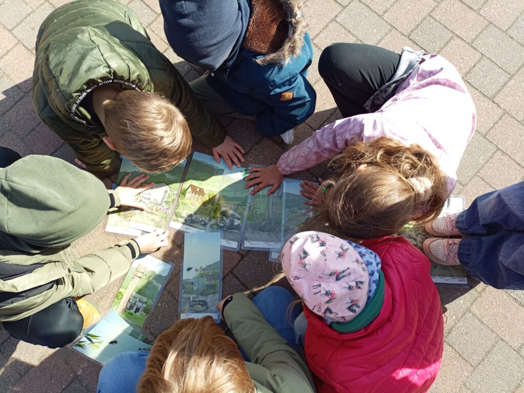 Sechs Kinder beugen sich über auf dem Boden liegende Abbildungen