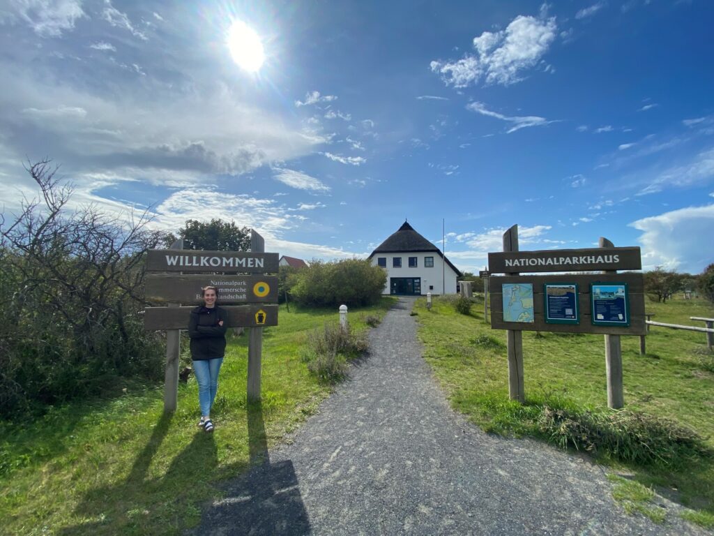 Die Praktikantin Aline Thiele lehnt an einem Schild "Nationalparkhaus" vor dem Nationalparkhaus der Vorpommerschen Boddenandschaft.