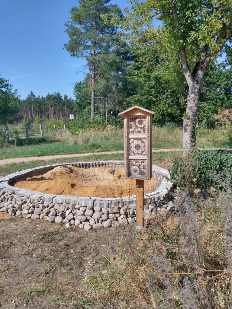 Sandarium in Lesesteinfassung, daneben ein Insektenhotel